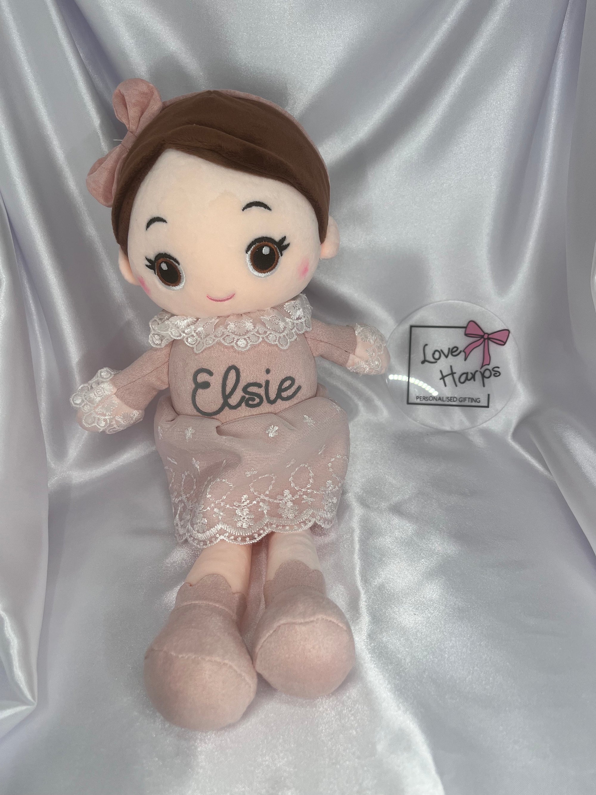 Plush doll named 'Elsie' with a pink dress and bow on a silver satin background